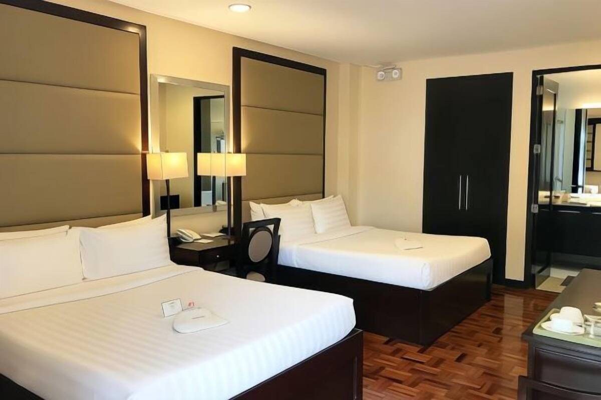 Habitación de hotel con dos camas, un espejo, una mesita de noche con lámpara, un teléfono y una pequeña mesa con una taza y un plato.