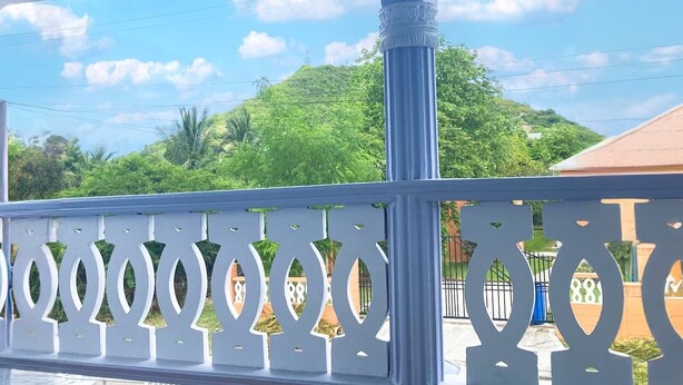 A covered outdoor area with a blue ceiling and white railings, overlooking a green landscape. - Sol Springs Estate (Osbourn)