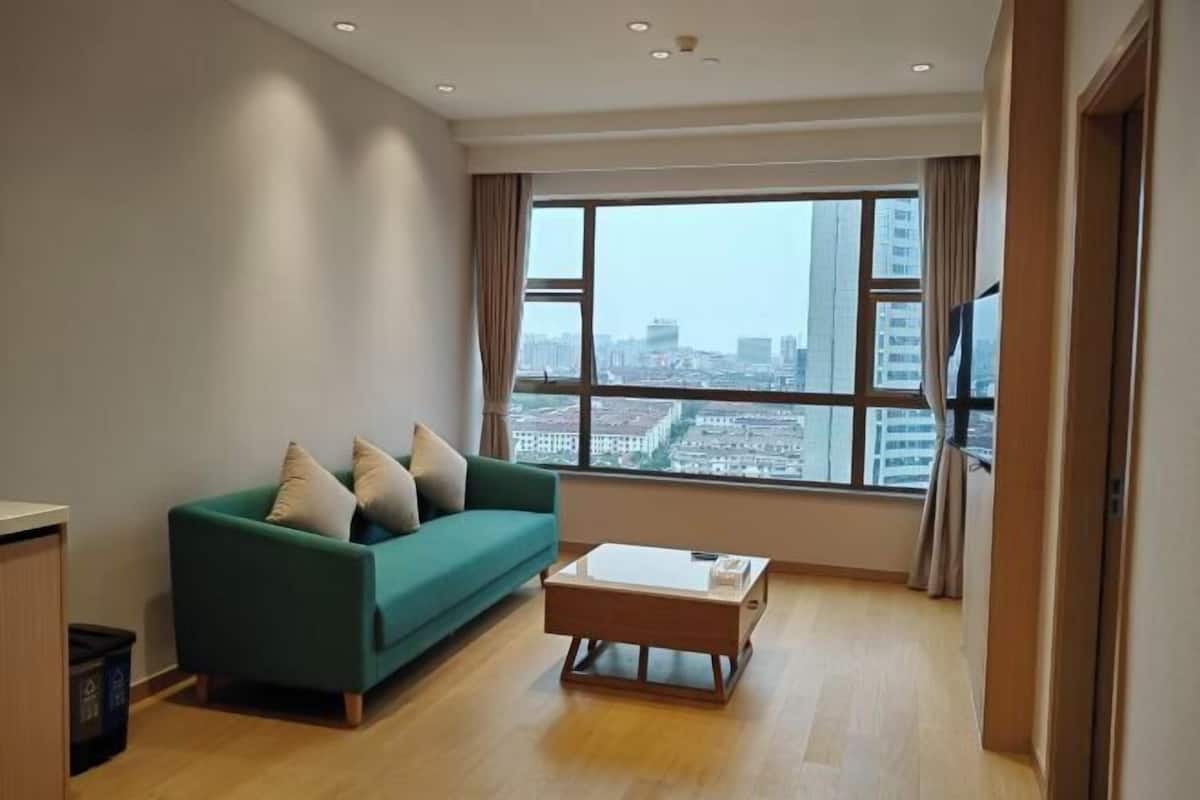 Een moderne woonkamer met een groene bank, een houten bijzettafeltje en een groot raam met uitzicht over de stad.