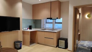 A compact kitchen with wooden cabinets, a built-in microwave, and a small window. - Guomao Boutique Hotel (Zhangjiagang)
