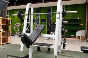 A gym with weightlifting equipment, a bench, and a green wall.