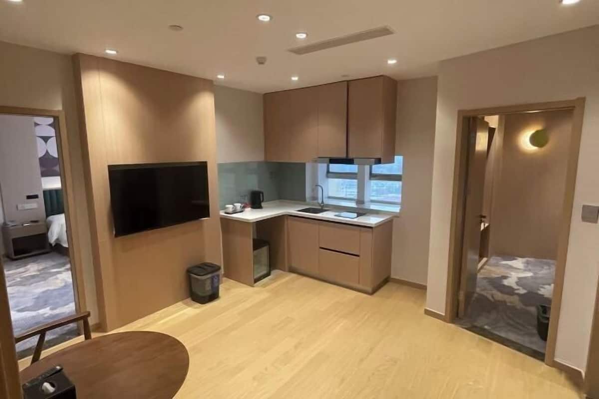 Een compacte hotelkamer met een kitchenette, een flatscreen televisie, een klein eettafeltje en een deur naar de badkamer.