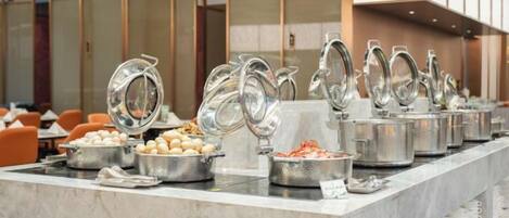 Un buffet avec plusieurs points de service, comprenant des plats présentés dans des récipients et des boissons chaudes.