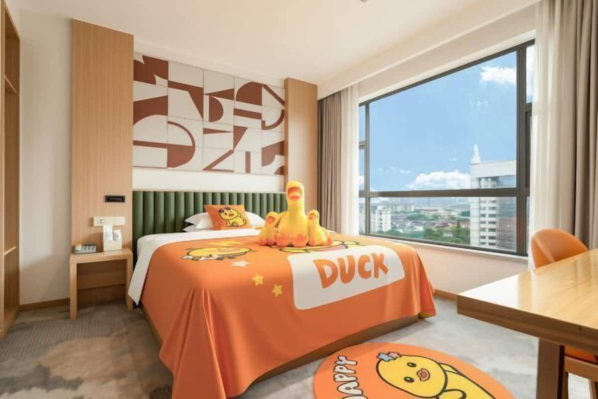 Hotelkamer met een bed, een tafel, een stoel, een nachtkastje, een raam met uitzicht en een stadsbeeld.