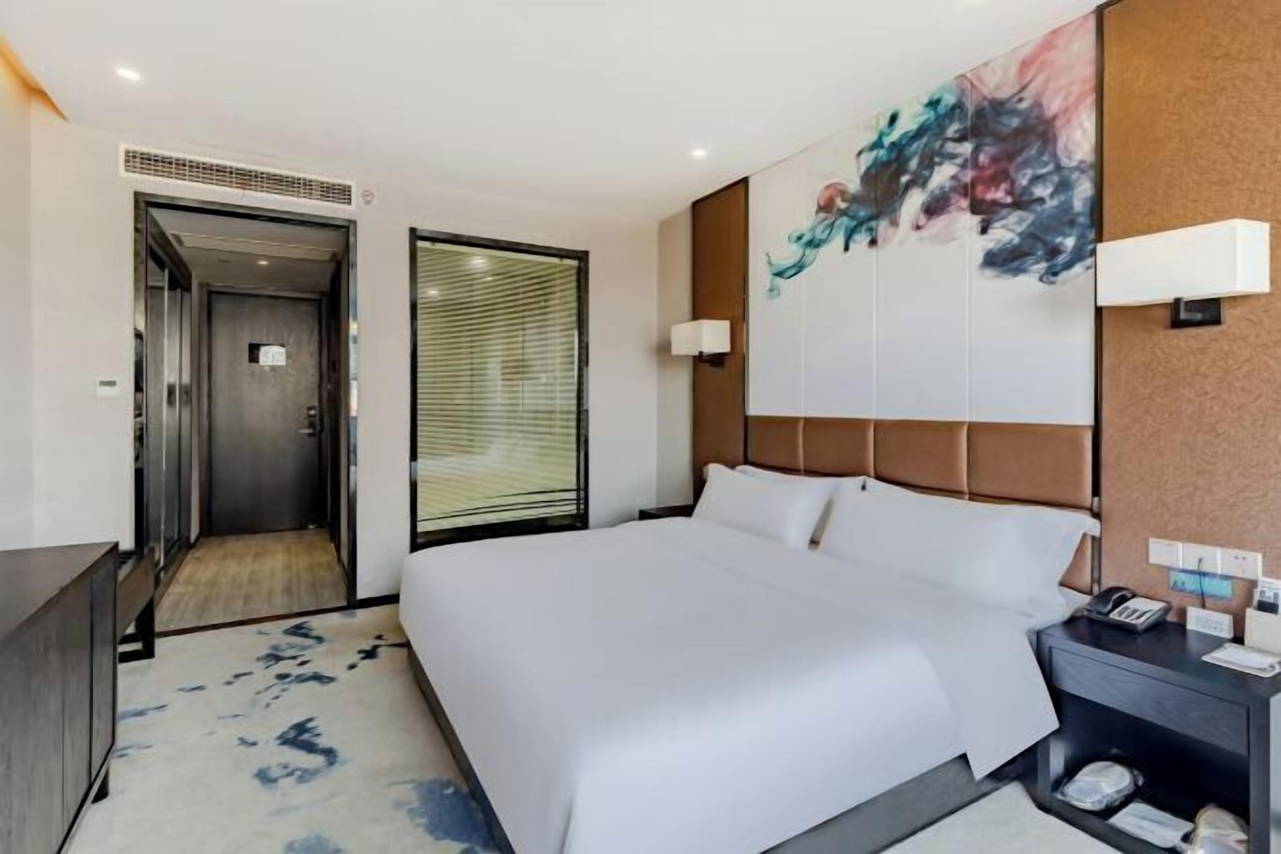 Una habitación de hotel moderna con una cama grande, una mesita de noche con teléfono, una lámpara de pared y un cuadro.
