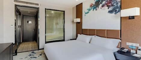 A modern hotel room with a large bed, a bedside table with a phone, a wall-mounted light, and a painting.