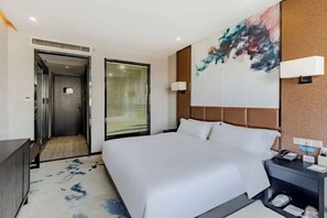 A modern hotel room with a large bed, a bedside table with a phone, a wall-mounted light, and a painting. - Hsh Cozy Hotel (Wuhu)