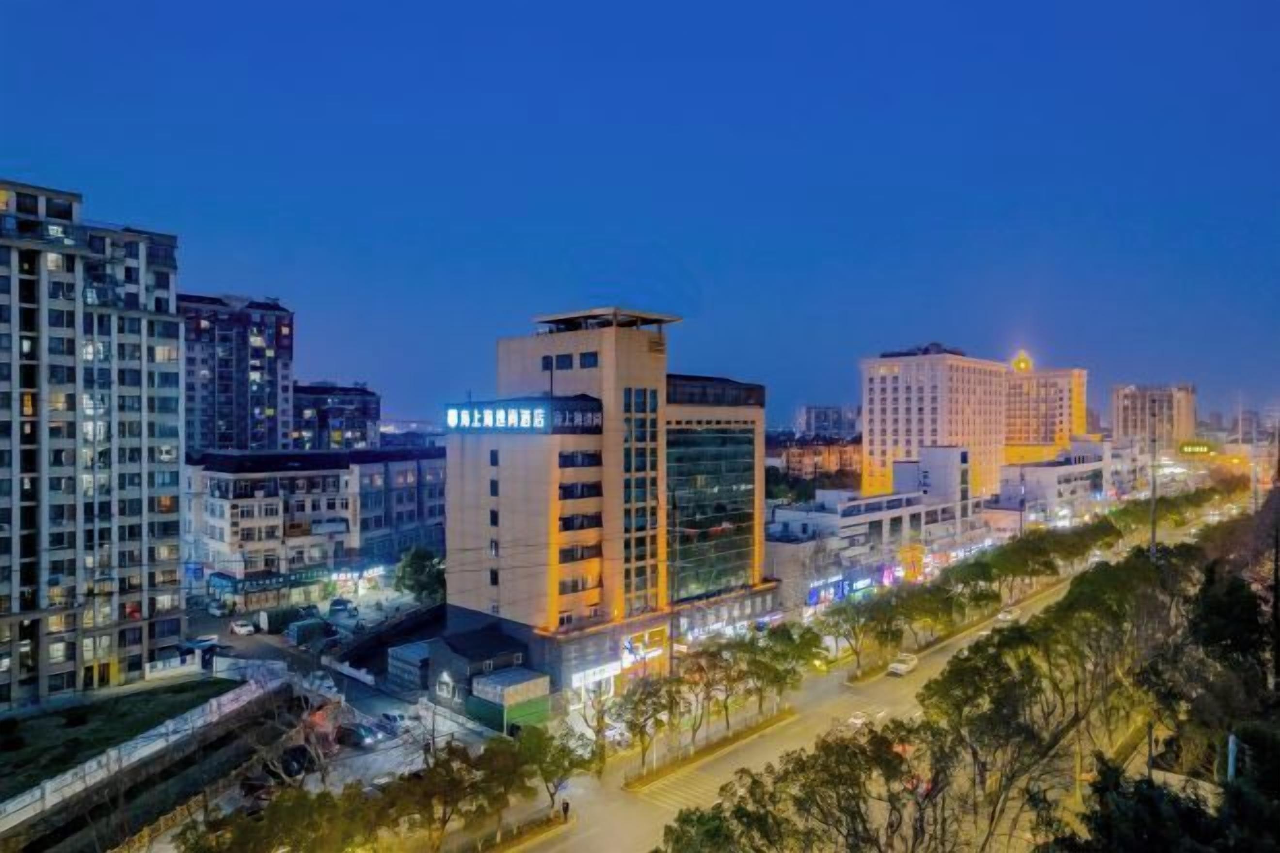 A cityscape at dusk with modern buildings, including a hotel with illuminated signage.