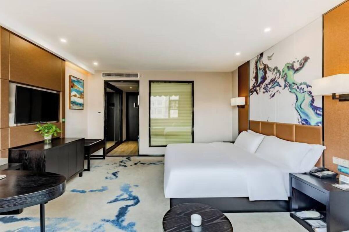 Quarto de hotel moderno com uma cama grande, uma escrivaninha, uma televisão e um quadro na parede.