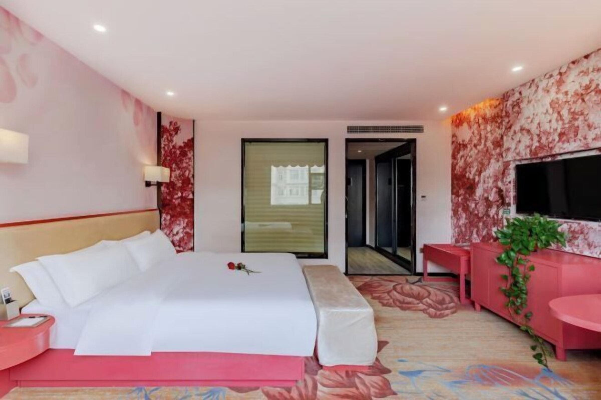 A hotel room with a bed, bedside table, TV, and a small seating area.