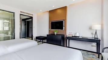 A hotel room with two beds, a desk, a TV, and a lamp.