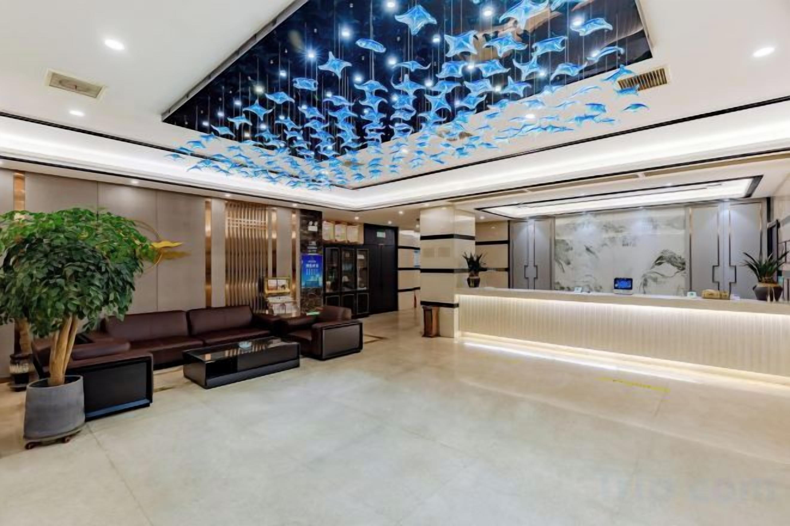 A hotel lobby with a reception desk, seating area, and a ceiling with hanging lights.