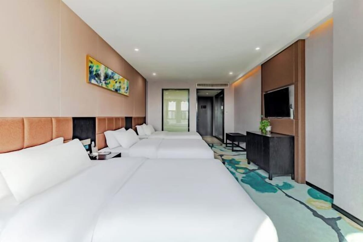 A hotel room with a large bed, a flat-screen TV, a desk, and a painting on the wall.