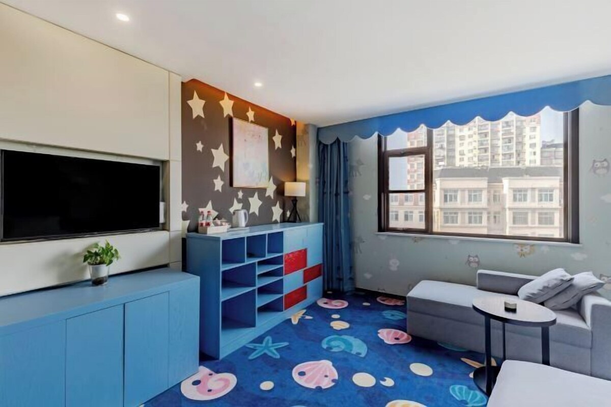 Una habitación moderna con un televisor grande, un sofá azul y una alfombra colorida con criaturas marinas.