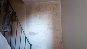 Un escalier avec une rampe menant à une pièce dont un mur est uni et présente une texture particulière.