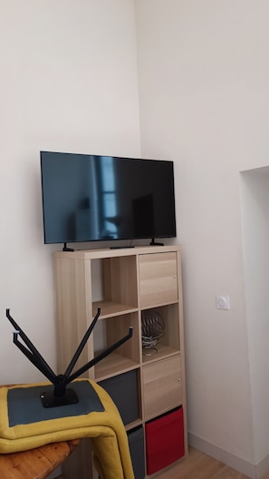 Un téléviseur posé sur un meuble en bois, une petite table avec une chaise et un interrupteur fixé au mur.