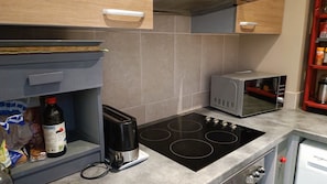 A kitchen with a black induction cooktop, a microwave, and a refrigerator. - Appartement T2 Intramuros Près Palais des Papes ds Hôtel Particulier (Avignon)