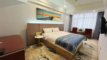 A hotel room with a large bed, a desk, a chair, a small table, and a painting on the wall.