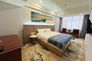 Habitación de hotel con una cama grande, un escritorio, una silla, una mesita y un cuadro en la pared.