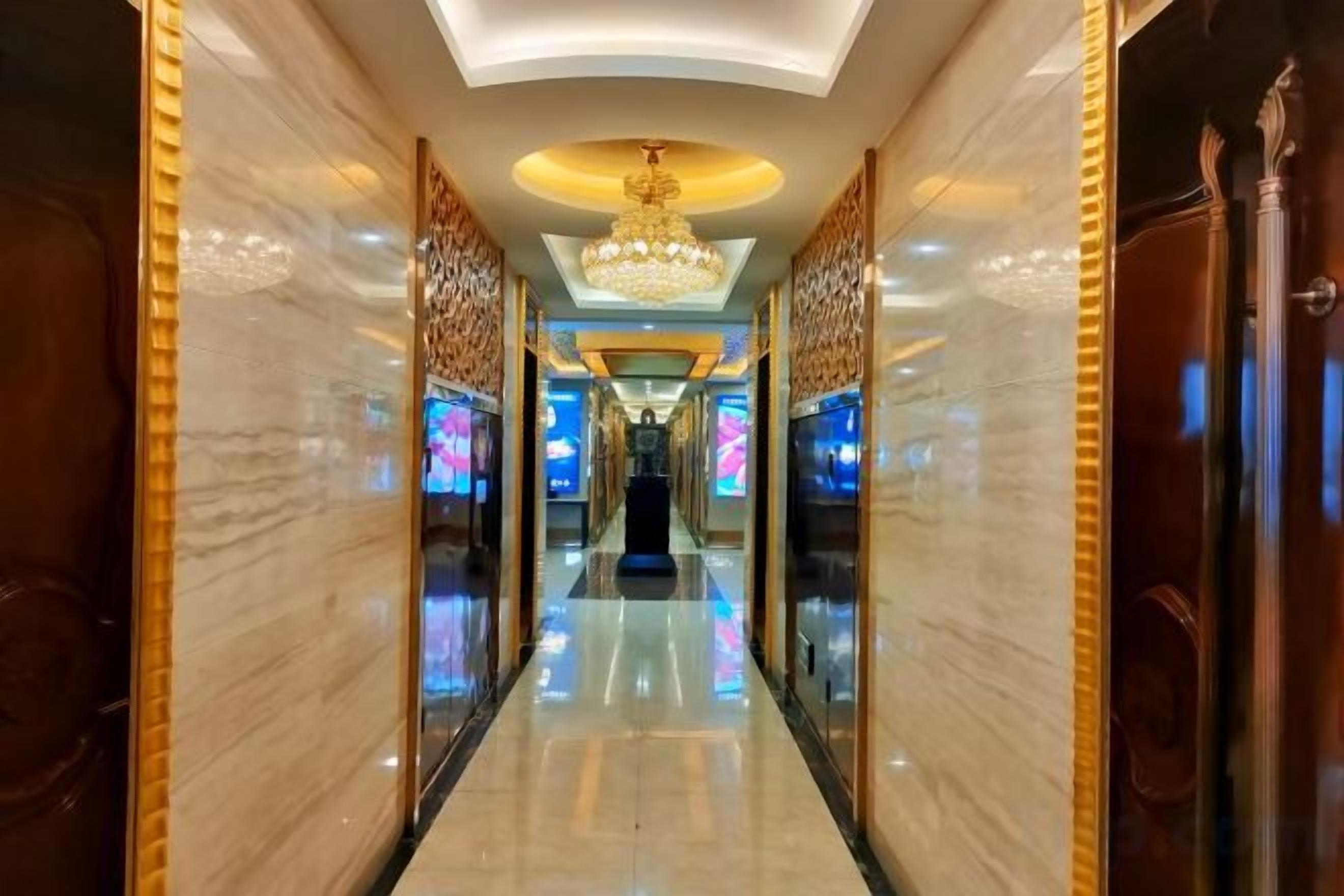 A hotel corridor with a chandelier, marble walls, and a reflective floor.