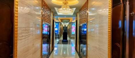 A hotel corridor with a chandelier, marble walls, and a reflective floor.