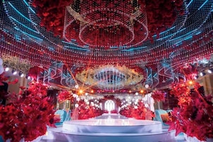 Un espacio de estar circular con una mesa central, rodeado de arreglos florales rojos e iluminación decorativa.