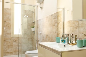 A modern bathroom with a glass shower enclosure, a white sink with teal accessories, and a marble-tiled wall.