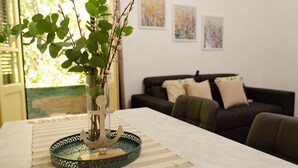 Ένα τραπέζι φαγητού με ένα διακοσμητικό κεντρικό στοιχείο, έναν καναπέ και έργα τέχνης στον τοίχο.