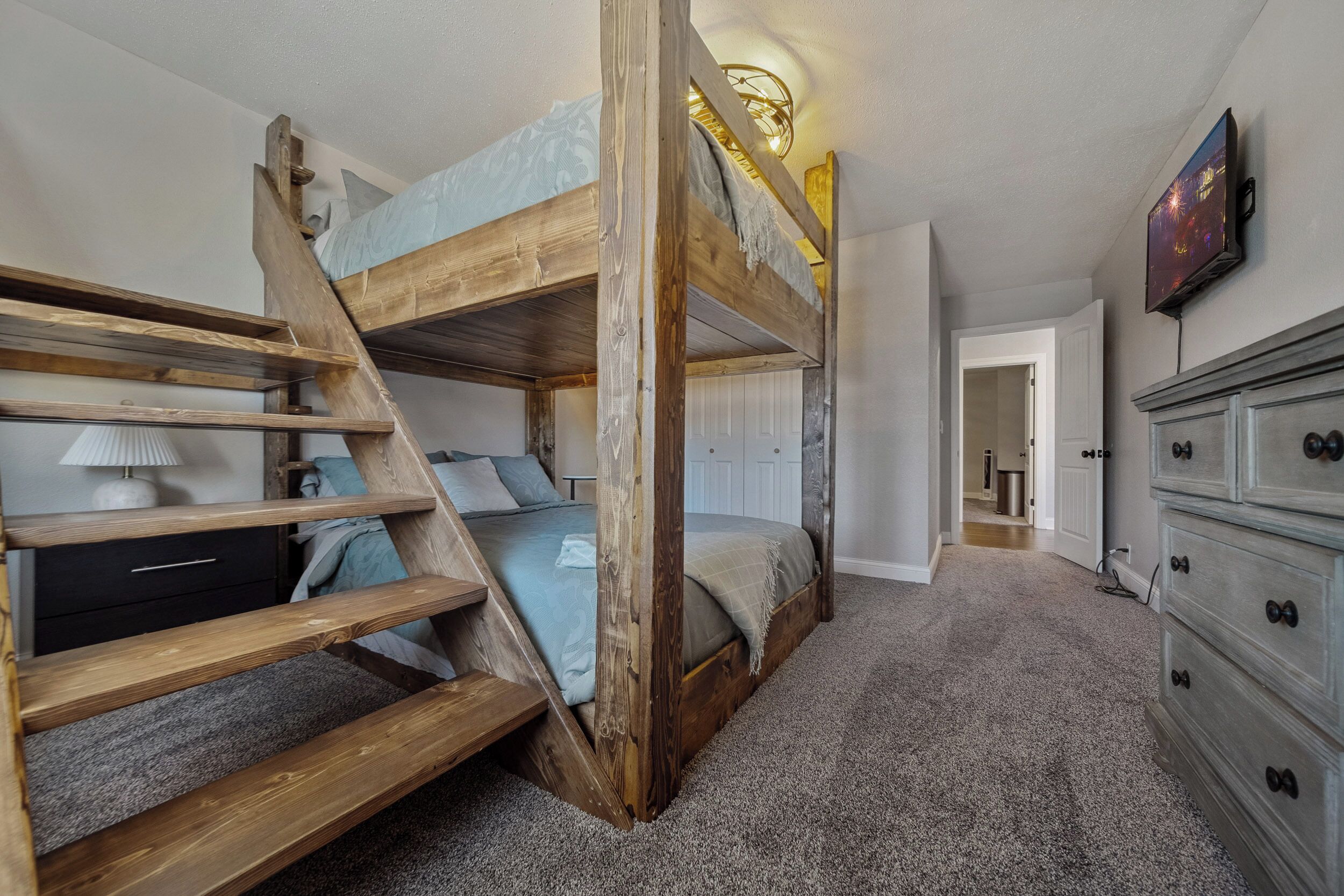A bunk bed room with a wooden ladder, a desk, and a dresser.