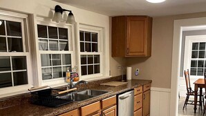 A kitchen with wooden cabinets, a granite countertop, a stainless steel sink, and a dishwasher. - 3 Bedroom house, close to the beach and beech forest. (Eastham)