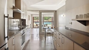 Una cocina moderna con electrodomésticos de acero inoxidable, vistas a la playa a través de amplios ventanales y un comedor con mesa y sillas.