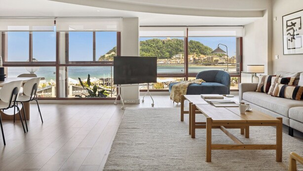 Un salón amplio con un gran ventanal que ofrece vistas al mar y a una colina.