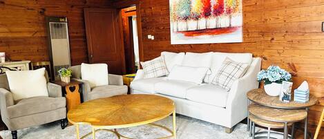 A living room with a white sofa, two armchairs, a coffee table, and a wooden floor.