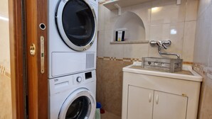Un espace buanderie compact comprenant une machine à laver et un sèche-linge superposés verticalement, une petite étagère pour les articles de toilette et un meuble avec un évier.