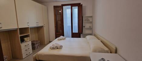 A hotel room with a bed, a bedside table, a wardrobe, and a shelf with a clock.