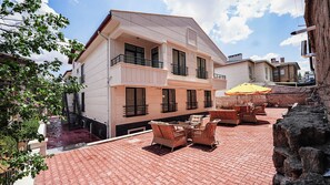 A multi-story building with a balcony, outdoor seating area with wicker furniture, and a brick-paved patio. - Cappadocia Ürgüp Apart Hotel (Ürgüp)
