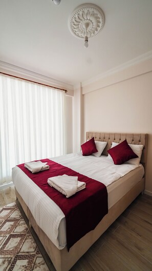 A neatly made bed with a red and white bedspread, two red pillows, and a beige headboard. - Cappadocia Ürgüp Apart Hotel (Ürgüp)