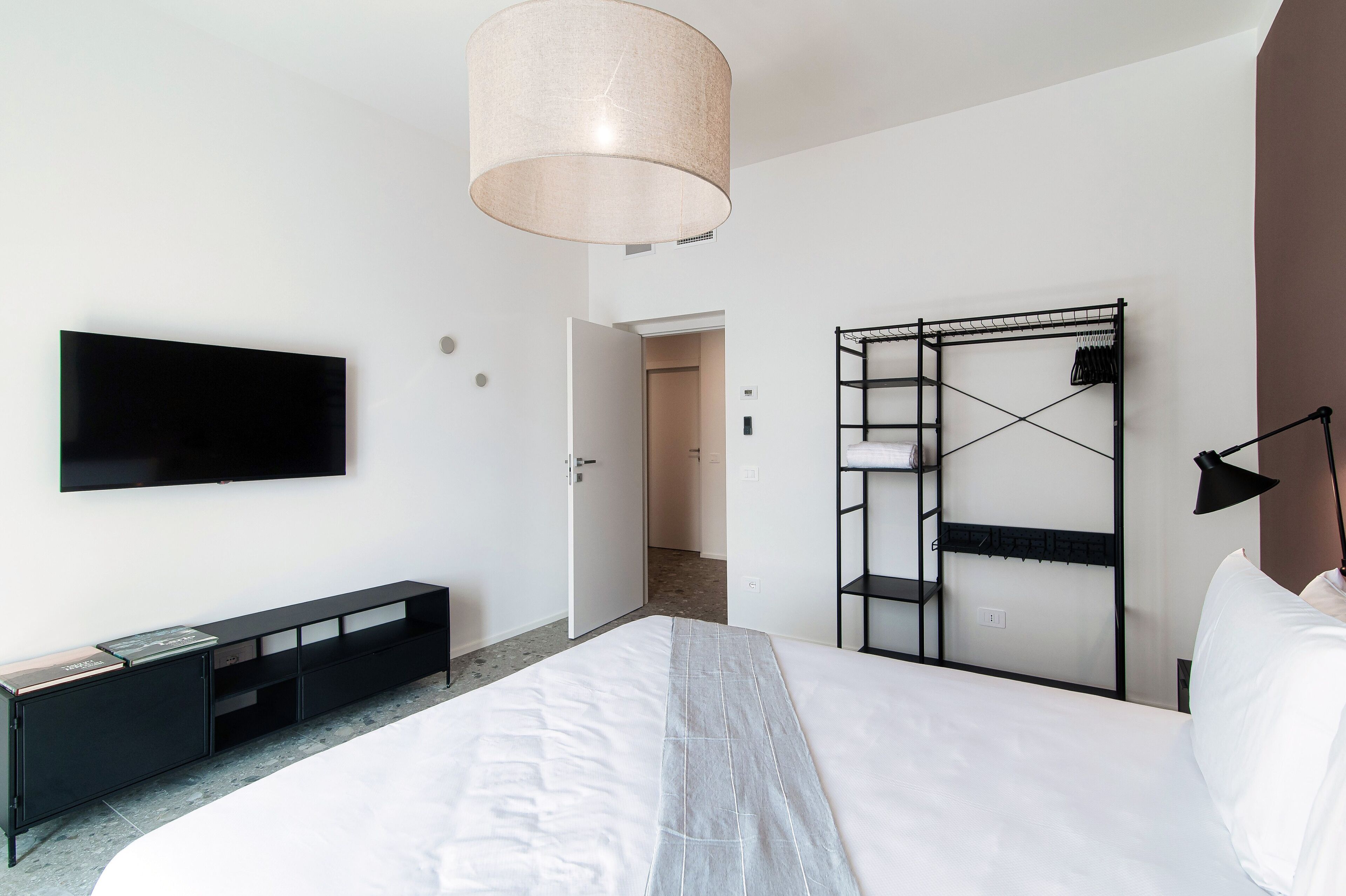 A modern hotel room with a large bed, a flat-screen TV mounted on the wall, a built-in wardrobe, and a bedside table.