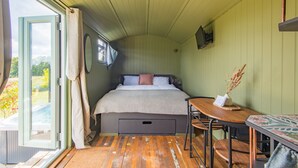Een slaapkamer met een bed, een tafel en uitzicht op een tuin door een open deur.