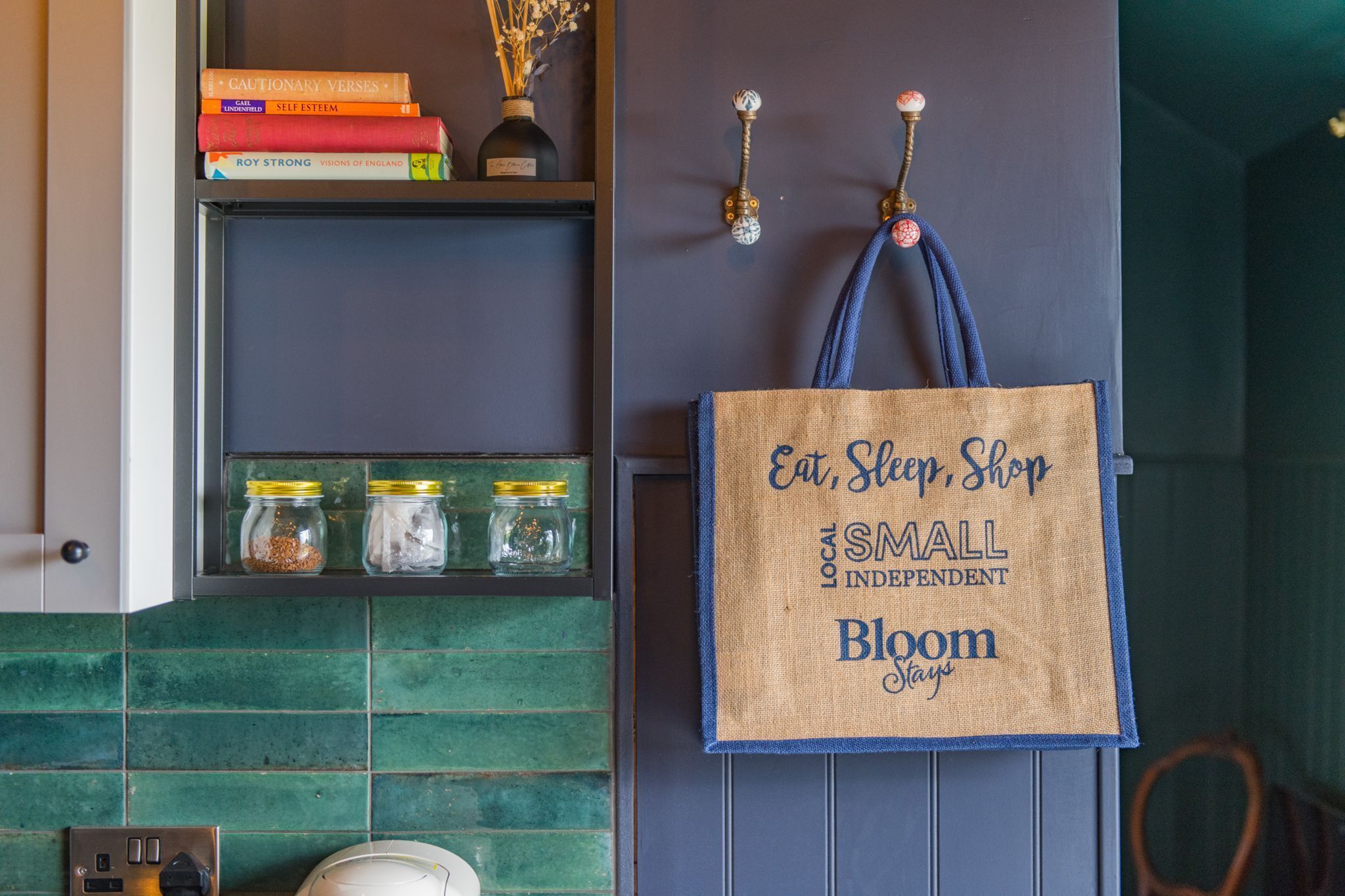 Una habitación con una estantería llena de libros y frascos, una puerta con una toalla colgada y una lámpara fijada a la pared.