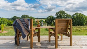 Een houten terras met twee stoelen, een tafel, een fles en een glas.