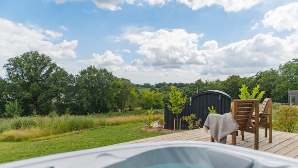A hot tub on a wooden deck with a view of a green landscape and a black shed in the background.