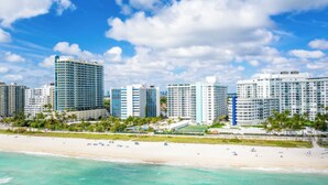 A beachfront hotel with multiple high-rise buildings, a sandy beach, and clear blue skies. - 2bd Oceanfront Master Ste OceanView w/balcony, Pool, nearby dining, beach access (Miami Beach)