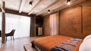 Ein Schlafzimmer mit Bett, Fernseher, Schreibtisch und einer Ziegelwand.