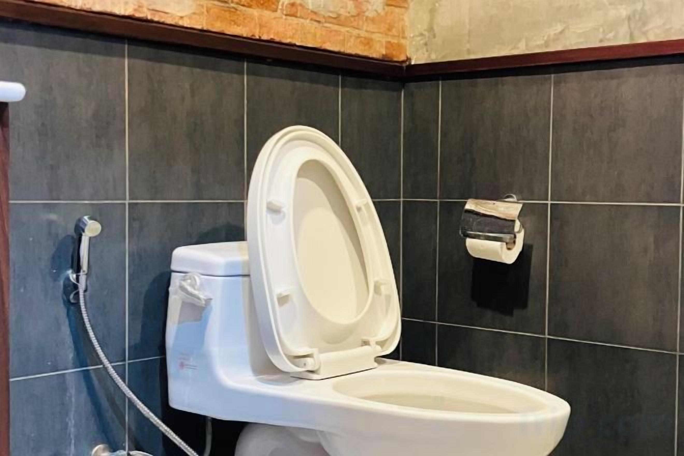 A white toilet with a closed lid, a toilet paper holder on the wall, and a shower head attached to the wall.