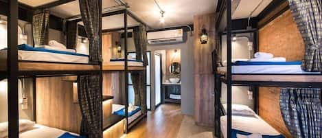 Habitación de hotel pequeña con literas, paredes de madera y un corredor central.