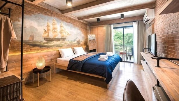 Ein Schlafzimmer mit einem Bett, einem Nachttisch, einer Lampe, einem Wandbild und einem Fenster.