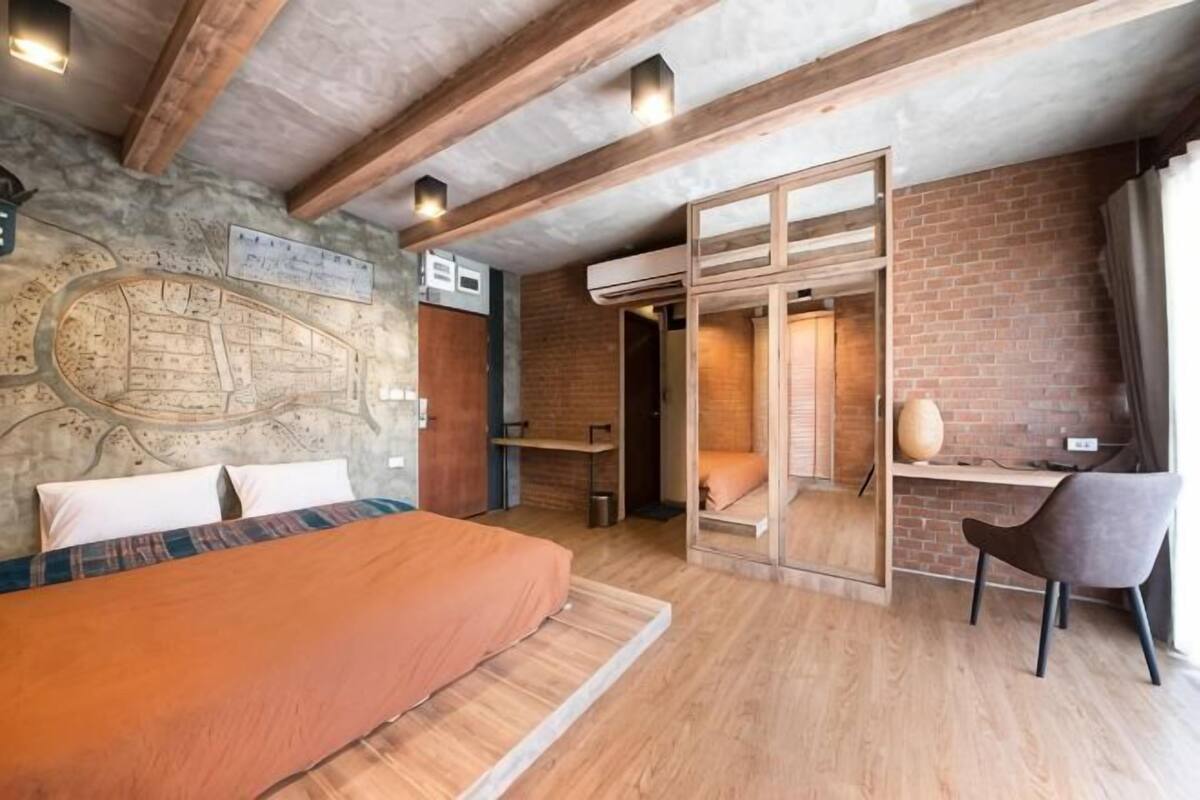 Ein Schlafzimmer mit Bett, Schreibtisch, Stuhl, einer Karte an der Wand und einer Ziegelwand.