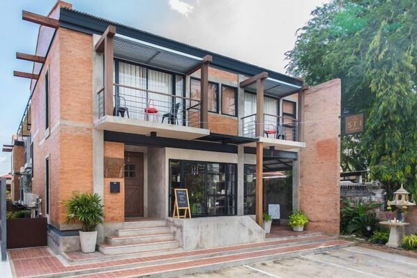 Un edificio de dos pisos con un balcón, un cartel con el número 51 y plantas en macetas en la entrada.