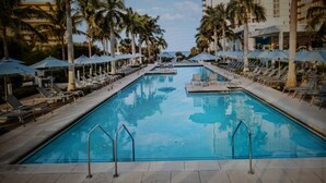 A swimming pool with lounge chairs and umbrellas, surrounded by palm trees and hotel buildings. - Charming 3-bedroom Gulf-view villa with many amenities in amazing Marco Island (Marco Island)